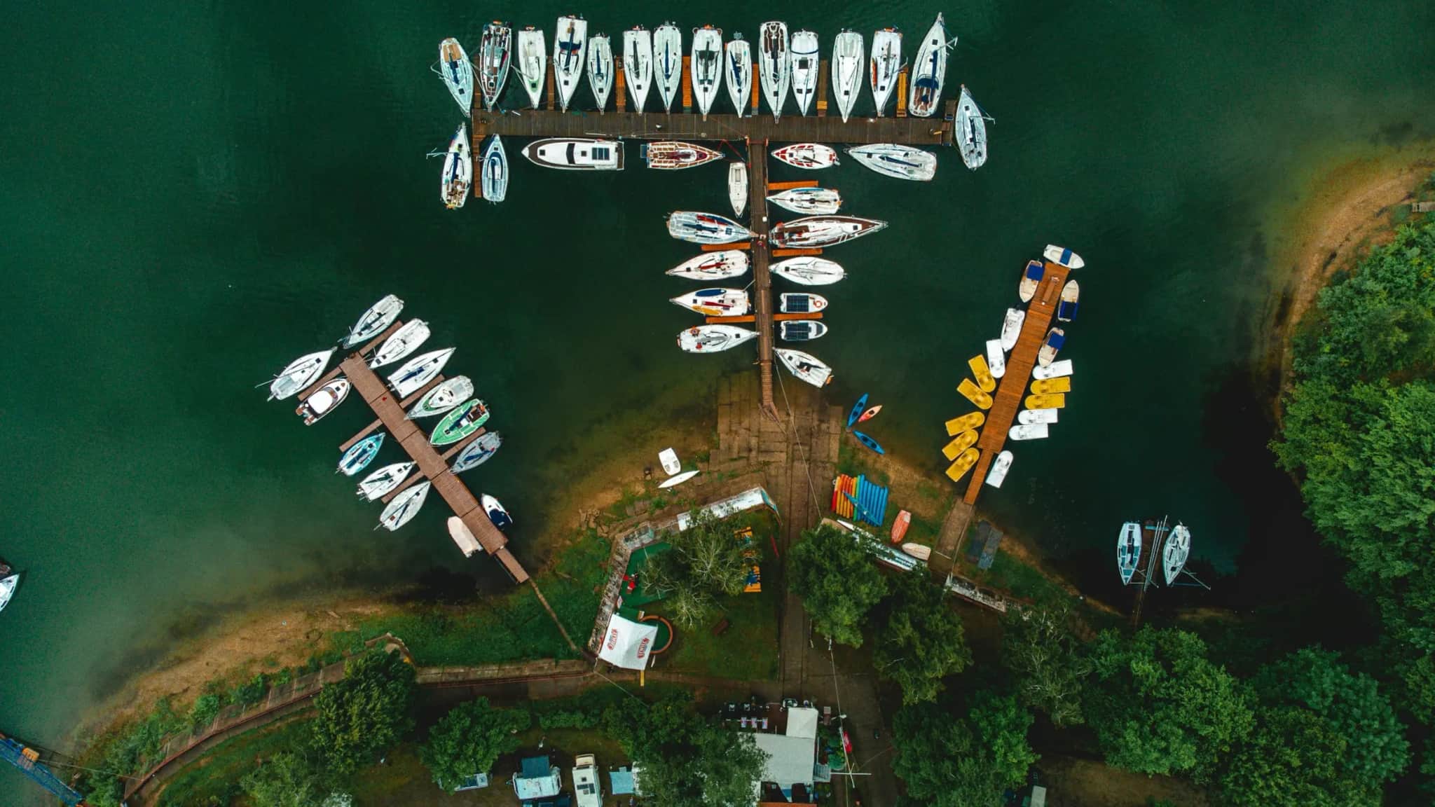 Czarter jachtów na Mazurach — marina z żaglówkami z lotu ptaka nad mazurskim jeziorem